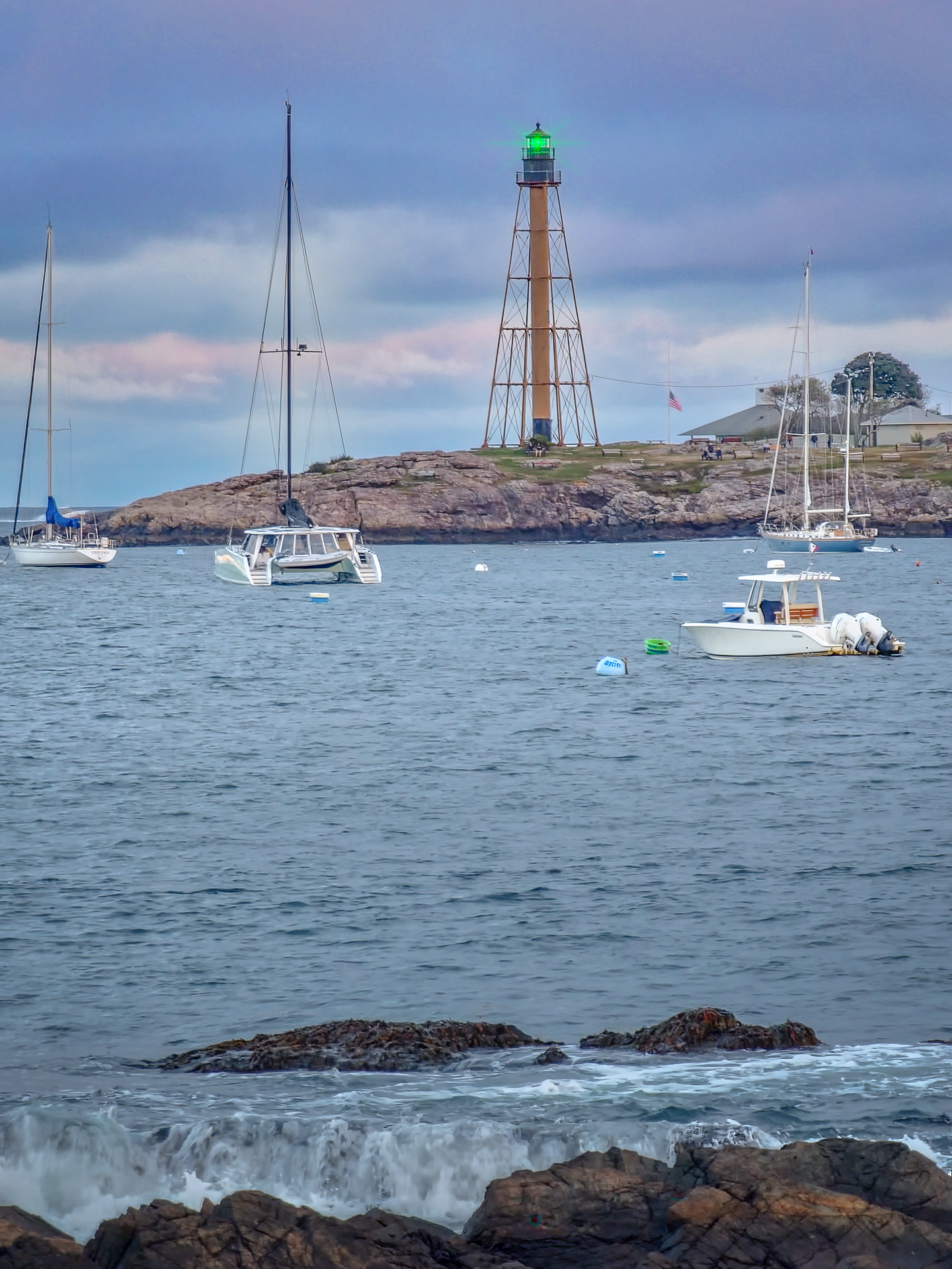Marblehead lighthouse at the harbor entrance with sailboats and rocky shoreline
